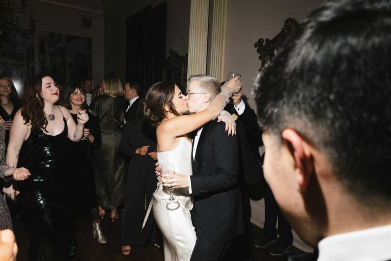 The couple shares a kiss on the dance floor surrounded by guests at their reception.