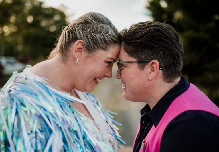 Two people smile with their foreheads together wearing matching hoop earrings and bright wedding outfits.