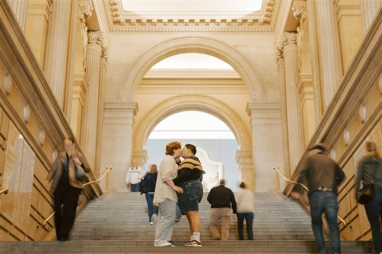 Two people kiss in the middle of The Met staircase as people move around them in the background.