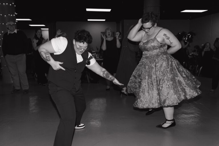 Sami strikes a dance pose while Kelsey spins beside her on the reception floor in black and white.