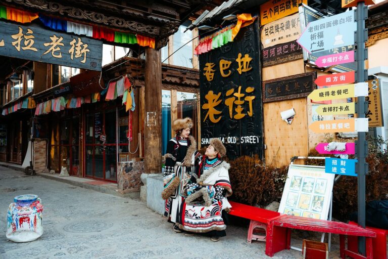 Two women in Tibetan-style coats stand in front of a sign reading Shangri-La Old Street.