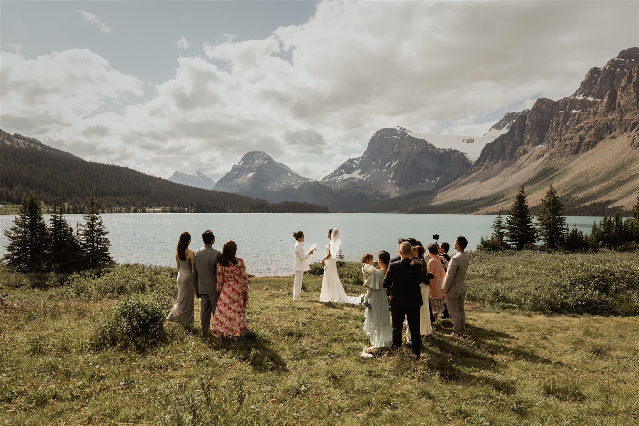Brides exchange vows by the lake as family and friends stand gathered around the ceremony site in Banff.