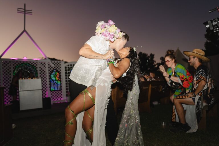 Partner dips bride in floral veil and green ribboned shoes while guests watch at festival ceremony.