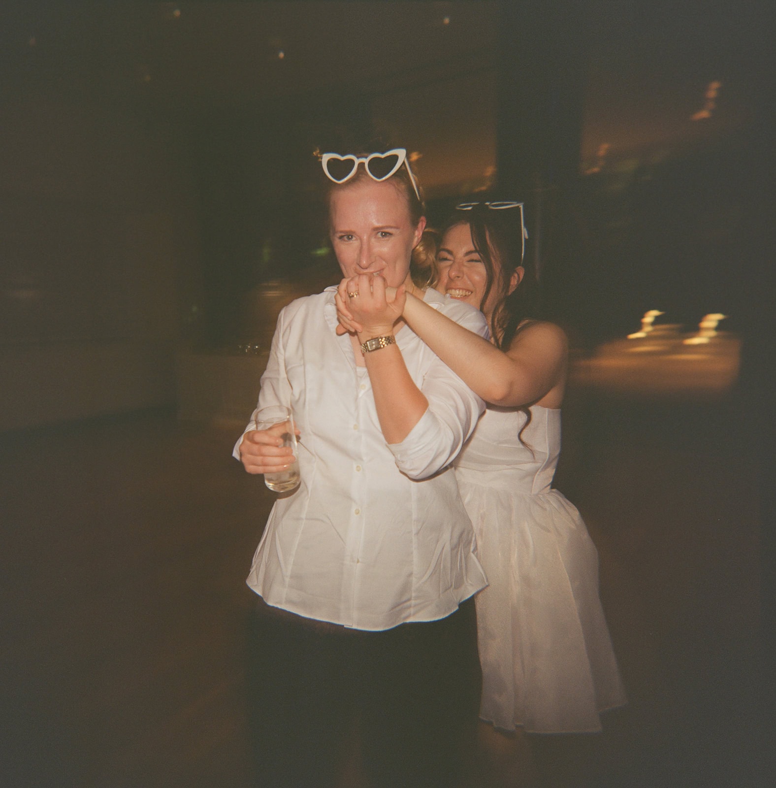 Bride in mini puff sleeve dress kisses hand of partner in shirt and trousers at reception.