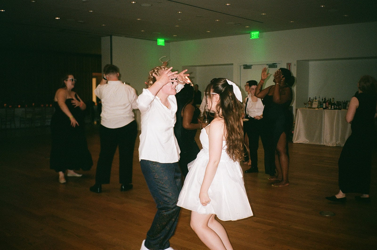 Bride in puff sleeve mini dress dances with partner in shirt and trousers on reception floor.