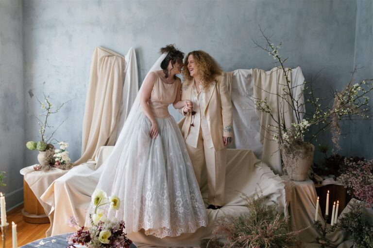 Two people laugh together while holding hands in Brooklyn studio, styled with florals and draped fabric.