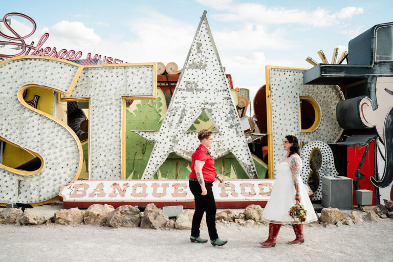 Two brides walk facing each other in front of a large star sign at the Las Vegas Neon Museum.