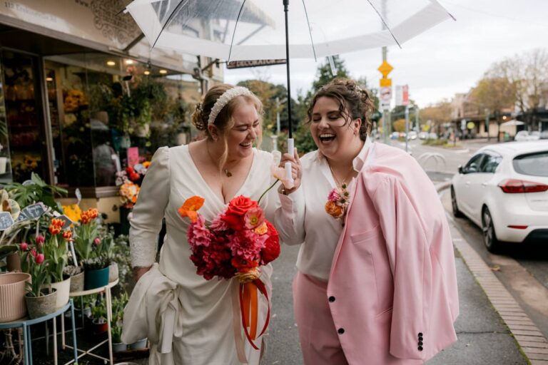 Queer couple laughing under clear umbrella outside a flower shop in Waterloo