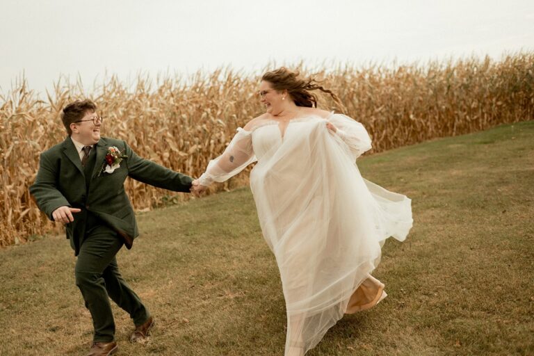 Queer couple running together by autumn cornfield